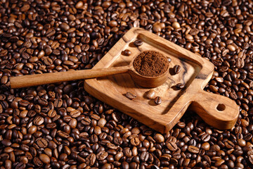 Naklejka premium Palone ziarna kawy z drewnianym podstawkiem i łyżeczką z mieloną kawą