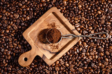 Obraz premium Palone ziarna kawy z drewnianym podstawkiem i łyżeczką z mieloną kawą