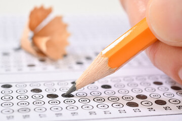 Student filling out answers to a test with orange pencil close-up   