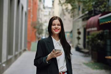 Fototapeta premium Woman smile with teeth with a phone in her hands walks around the city fashion on the street, spring travel, vacation in the city tourist freelancer