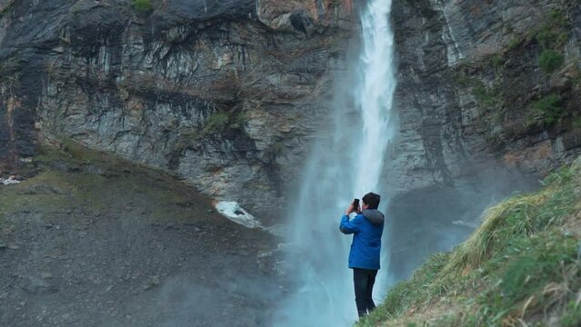 Young Indian man tourist standing against beautiful Sissu waterfall. Tourist taking photo, pictures of Sissu waterfall at Lahaul, Himachal Pradesh, India. Travel tourism concept 