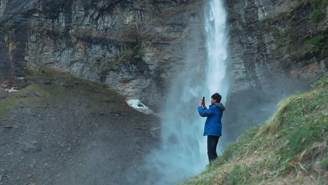 Young Indian man tourist standing against beautiful Sissu waterfall. Tourist taking photo, pictures of Sissu waterfall at Lahaul, Himachal Pradesh, India. Travel tourism concept 