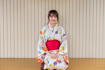 Fototapeta premium Young woman wearing traditional kimono sitting in Japanese style house with tea set with garden background