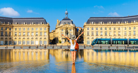 Happy woman tourist with arms raised in France- Bourse square with water mirror,  Bordeaux city...