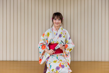 Young woman wearing Japanese traditional kimono holding paper fan sitting in Japanese style wooden house