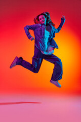 Fototapeta na wymiar Portrait of emotive, young girl wearing casual clothes jumping in air over red color studio background in neon light. Levitating dreamer