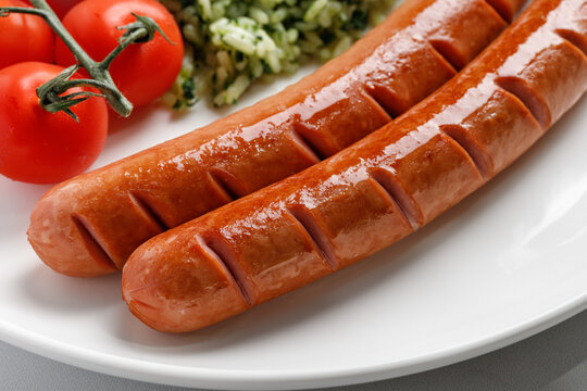 Two fried delicious sausages and side dish, tomatoes cherry on white plate. Dinner dish idea. Close up.
