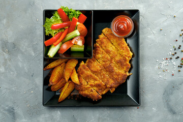 Austrian chicken schnitzel with potatoes and salad on a black plate