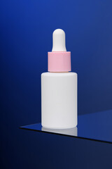 In the blue background, a bottle of serum stands on glass.  Vertical advertising photo of cosmetics. Mockup. Template.