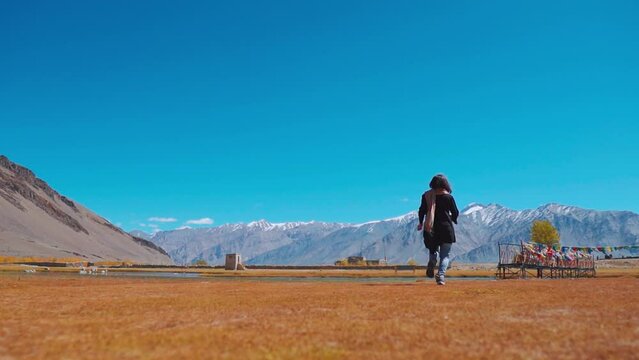 Slow motion shot of happy woman hiker jumping against blue sky and mountains in background at Sani village, Zanskar. Travel and active lifestyle concept. Girl jumping with happiness. Travel in Summer