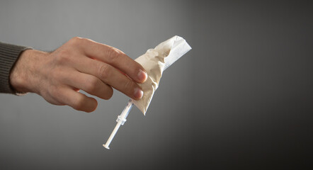 Male hand showing syringe and plastic packet of heroin.