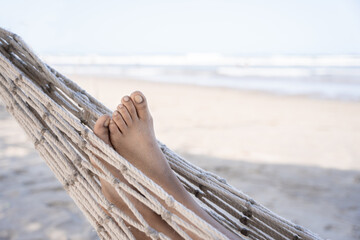 A close-up of a young Hispanic woman's sandy feet as she lounges on a hammock at the beach.