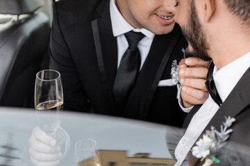 Cropped view of positive gay groom with braces in classic suit touching chin of bearded boyfriend...