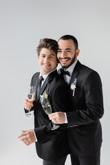 Portrait of positive same sex couple in elegant classic suits holding glasses of champagne while...
