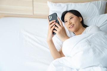 Closeup portrait of young sleepy exhausted woman lying in bed using smartphone