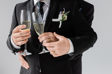 Cropped view of gay couple in classic suits and golden rings holding glasses of champagne while...