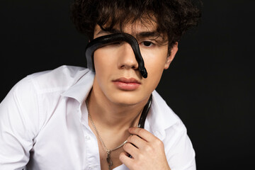Young handsome man in a white shirt with a black snake crawling on his face. Isolated on black background.