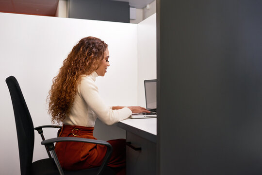 Side view of multi-ethnic woman working in private cubicle, coworking office