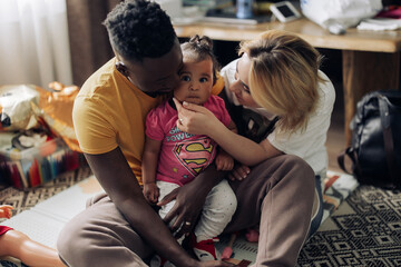 Happy interracial family plays in room with their baby daughter.