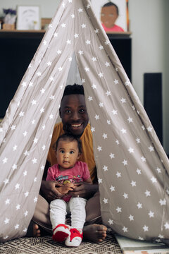 Young African man plays with his little mixed race daughter in baby tent .
