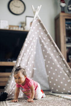 Baby mixed race girl crawls and plays in room against background of tent.