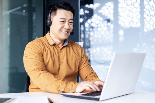 Happy and smiling worker with headset for video call, Asian tech support man talking to online service users, businessman using laptop for online customer support