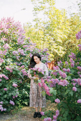Young woman walks in garden with bouquet and enjoys by blooming lilac shrubs.