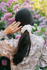 Naklejka premium Back view to brunette woman enjoying by blooming lilac shrubs.