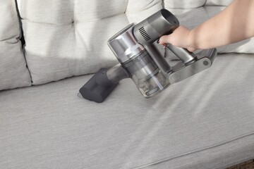 A woman vacuums a white sofa with a cordless vacuum cleaner.