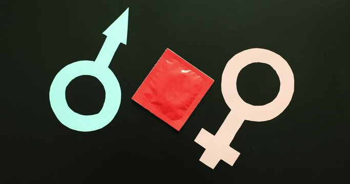 Hand of woman putting condom in red package between male and female symbols on black background. Intimate relationship between man and woman
