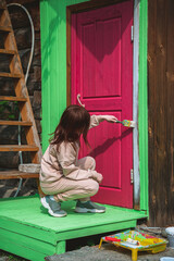 Cute girl painting the door of a wooden house in a bright purple viva magenta color