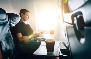 Fotobehang Oud vliegtuig Brunette 40 years old female airplane passenger with tablet in hands sitting in comfortable seat near the window. Attractive woman enjoying flight while using with touch pad online connection on board