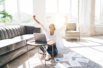 Cheerful woman with laptop raising arms up in glee gesture