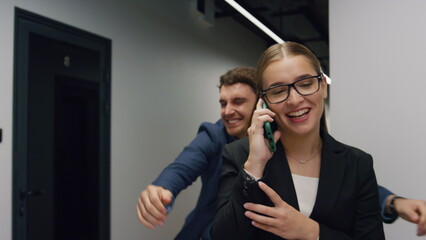 Office girl talking mobile phone going hall. Handsome man colleague embracing