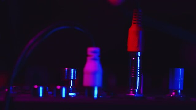 DJ carefully connecting plugs into sockets on a mixer during the studio recording session in a color light close up. Electronic musician plugging audio equipment