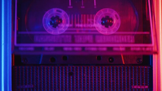 Audio engineer puts an audio cassette into a professional tape recorder and starts the recording during the studio session in a color light in the view from above close up