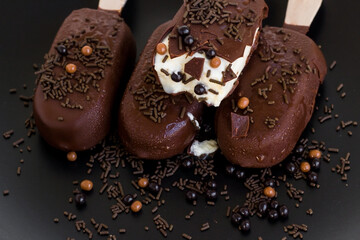 Melted and bitten ice cream with wooden sticks, cocoa with decorative candies on black surface
