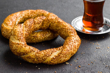 Traditional Turkish crispy,sesame bagels and a glass of tea on the black surface with sesame seeds