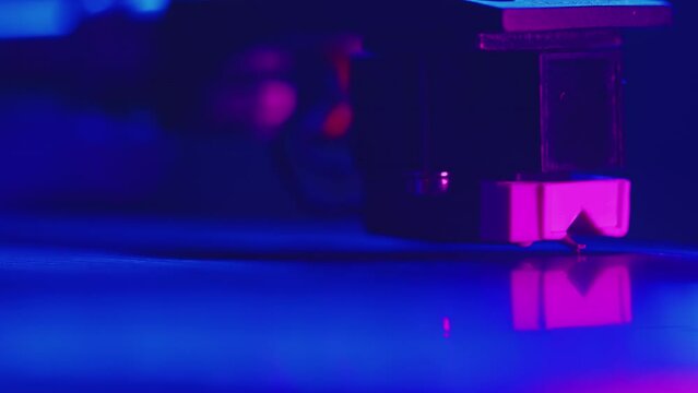 DJ puts the needle of the headshell of the turntable on the surface of the record close up, and the record starts to rotate during the studio recording of the vinyl session in a color light