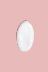 A dab of cosmetic cream. Light, smooth surface. Texture of spreadable cream. Liquid cream smear. On a pink background.