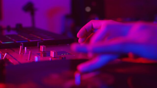 DJ carefully uses the crossfader on the mixer when mixing a track from a vinyl record during the studio recording session in a color light close up