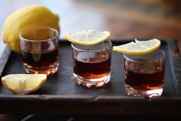 three shot glasses with lemon slices on a wooden plate
