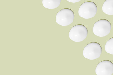 Lots of smears of cosmetic cream. Light, smooth surface.  In a row. At an angle. Top view. Texture of flowing cream. Liquid creamy strokes. On green background. Cosmetic background, banner.