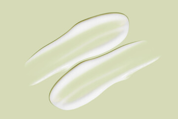 Lots of smears of cosmetic cream. Light, smooth surface.  In a row. At an angle. Top view. Texture of flowing cream. Liquid creamy strokes. On green background. Cosmetic background, banner.