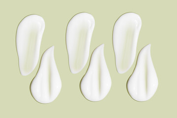 Lots of smears of cosmetic cream. Light, smooth surface.  In a row. At an angle. Top view. Texture of flowing cream. Liquid creamy strokes. On green background. Cosmetic background, banner.