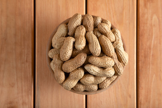 Bowl full of shelled peanuts on wooden background,top view
