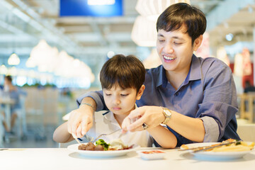 Happy cheerful Asian man and lovely little son enjoy eating a food in the fast food restaurant...