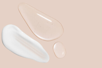 Obraz premium Drops of transparent gel and a dab of white cosmetic cream. On a beige background.