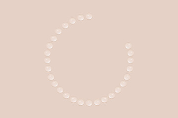 Drops of transparent gel or water are arranged in the shape of a not full circle. On a beige background.