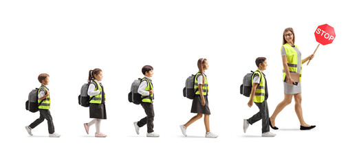 Female teacher leading schoolchildren in safety vests, carrying a stop sign and walking